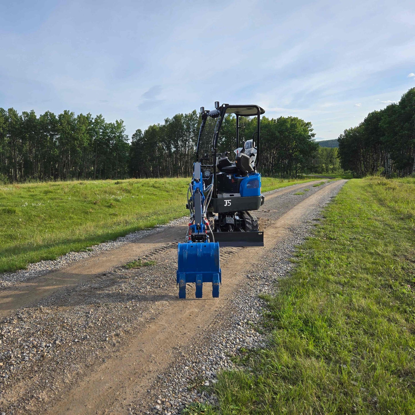 Rippa R18 Mini Excavator for sale JoyT5 | rear angle view on a gravel road with blue digging bucket in a natural green environment