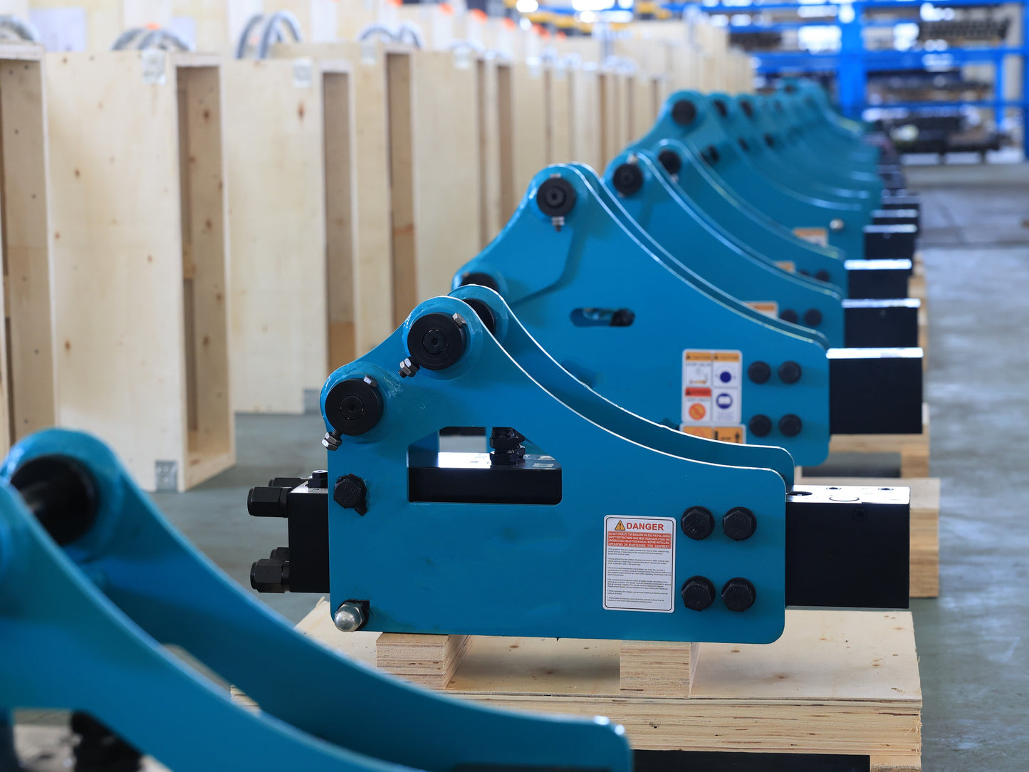Multiple blue JoyT5 excavator hydraulic breaker hammer attachments lined up in factory on wooden pallets
