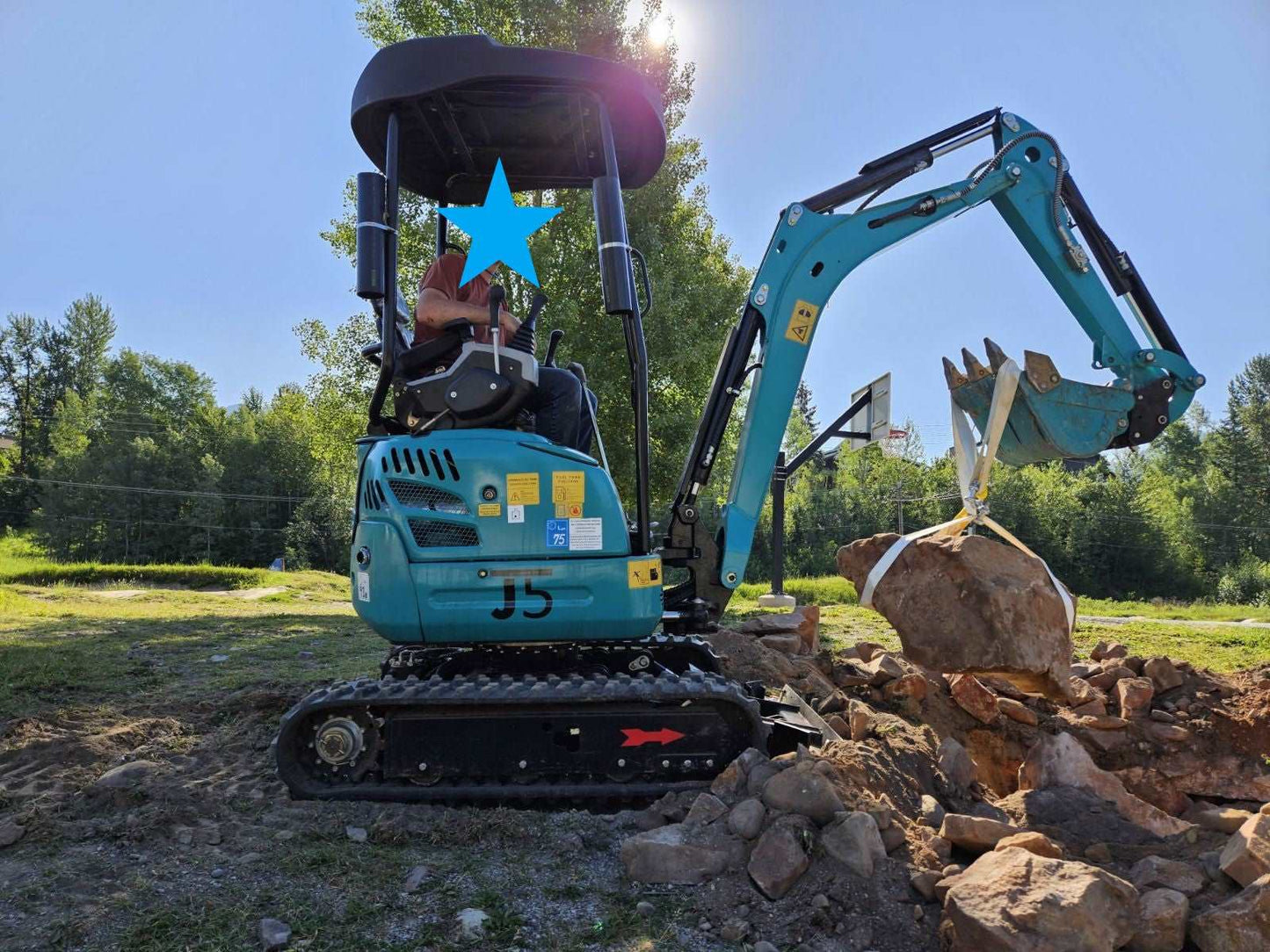 JoyT5 mini excavator lifting large rock with bucket attachment during landscaping and construction project in Calgary Alberta