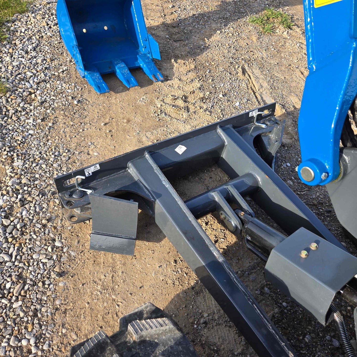 Close-up view of JoyT5 Rippa R18 Mini Excavator front blade and detached blue digging bucket on gravel ground