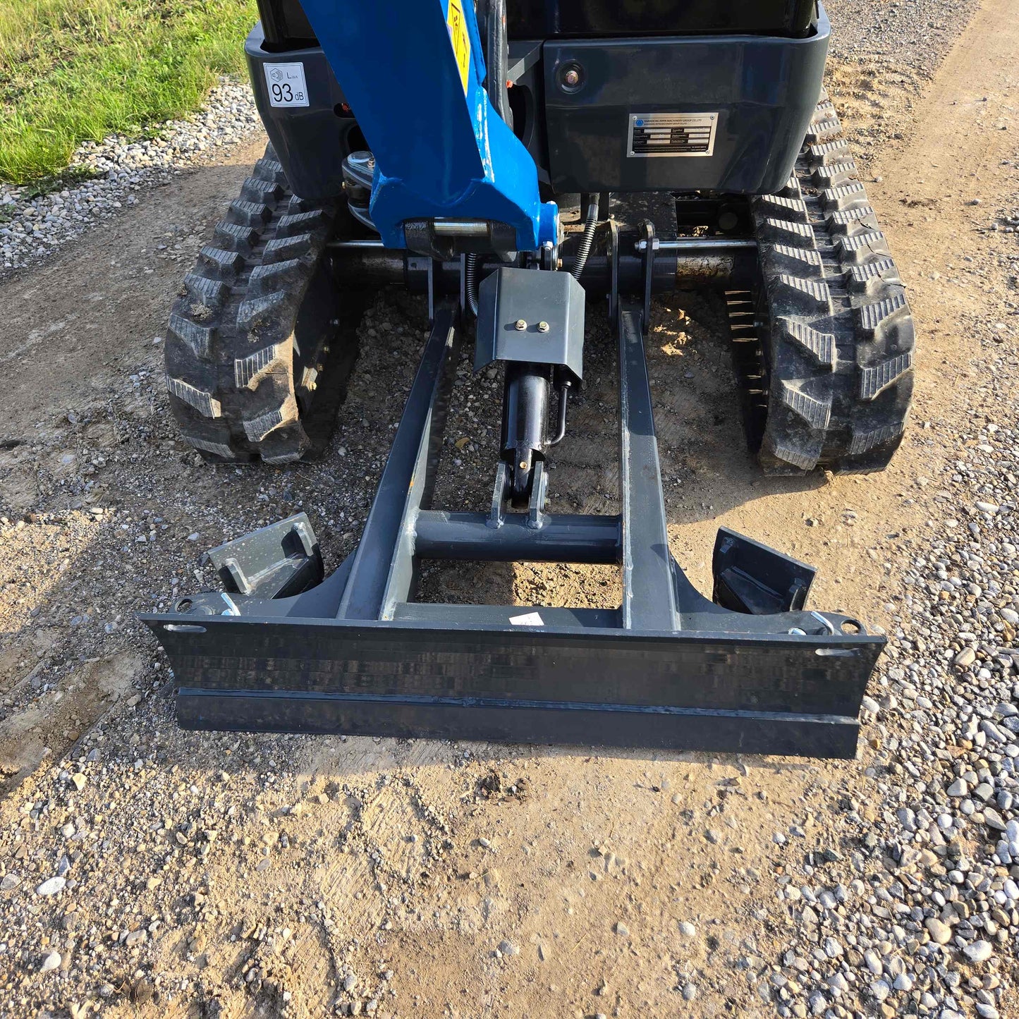 Close-up view of JoyT5 Rippa R18 Mini Excavator front dozer blade with hydraulic cylinder and rubber tracks on gravel surface