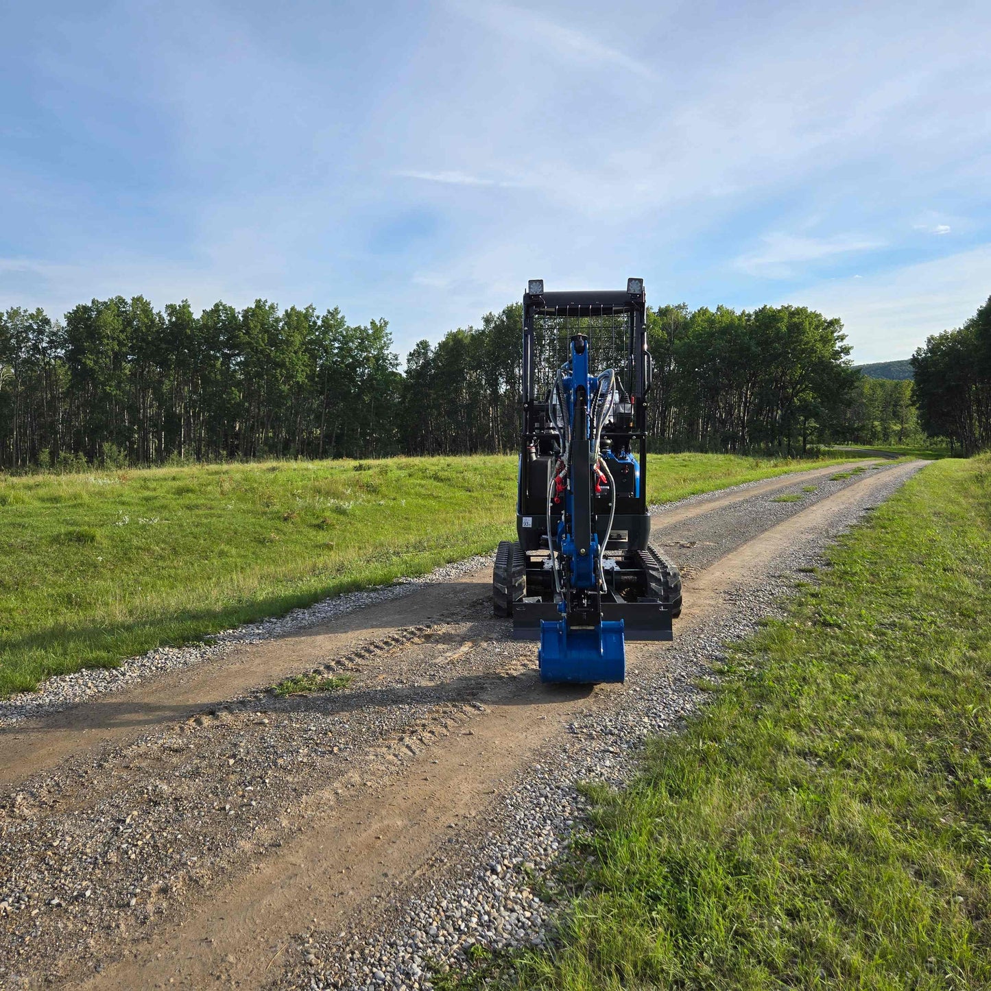 Front view of JoyT5 Rippa R18 Mini Excavator on gravel road with green grass and forest background