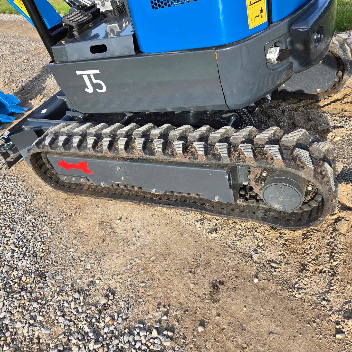 Close-up side view of JoyT5 Rippa R18 Mini Excavator rubber track with a red arrow indicating direction on gravel surface