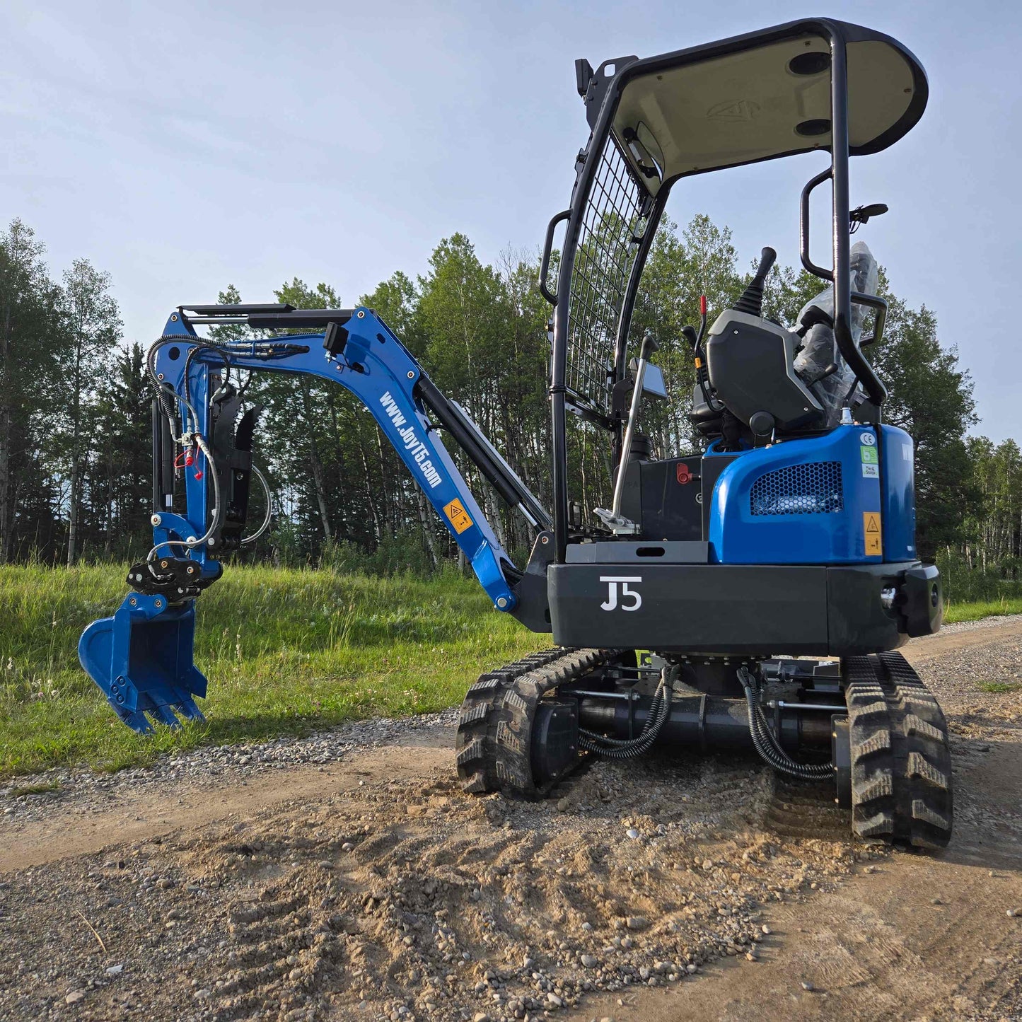 Side rear view of JoyT5 Rippa R18 Mini Excavator with digging bucket lowered and rubber tracks visible on gravel surface