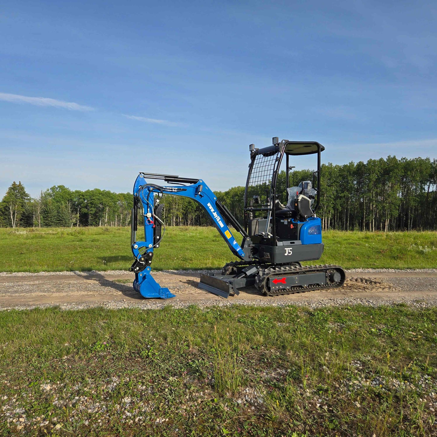 Side view of JoyT5 Rippa R18 Mini Excavator with bucket resting on ground, rubber tracks and front blade visible on gravel path