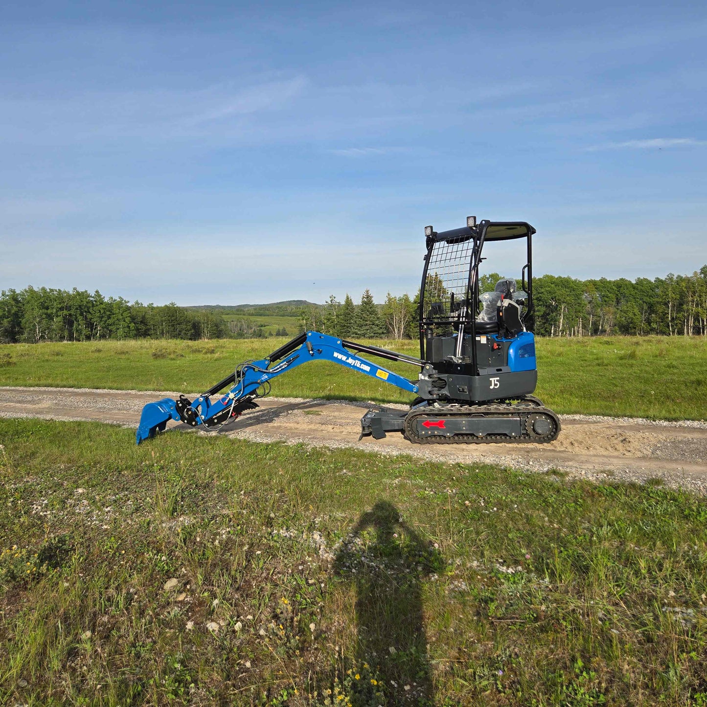JoyT5 Rippa R18 Mini Excavator side view with arm lowered working on dirt road in rural landscape