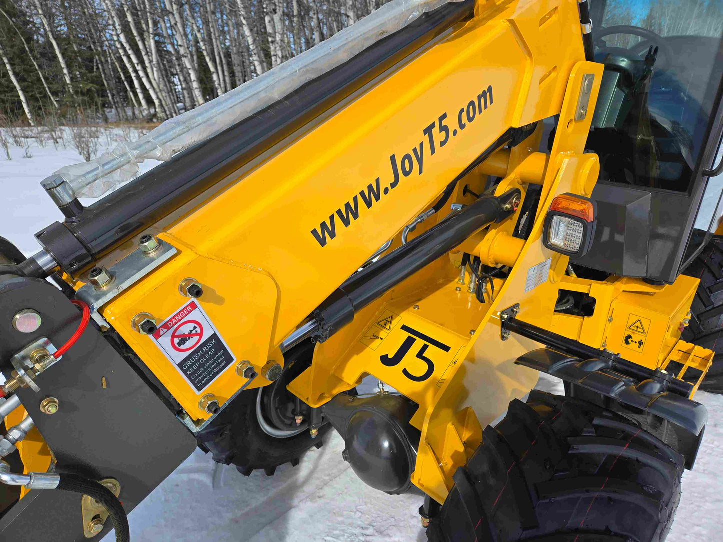 Close-up of JT5WL1000 mini wheel loader arm with hydraulic cylinder and warning label for safe operation.