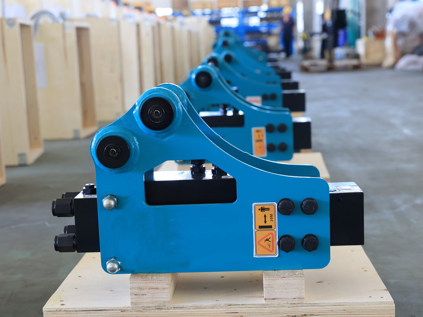 Multiple JoyT5 blue excavator hydraulic breaker hammer attachments arranged in factory storage.