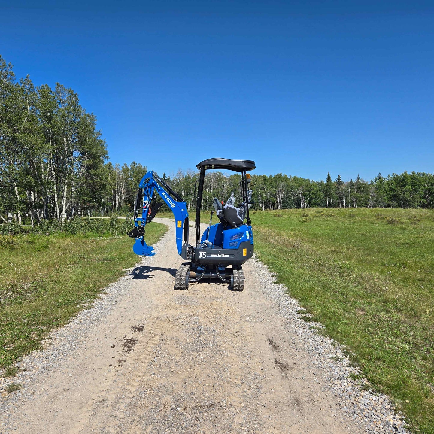 Rippa R15 Mini Excavator For Sale – rear view of compact digger on gravel road with green countryside background.