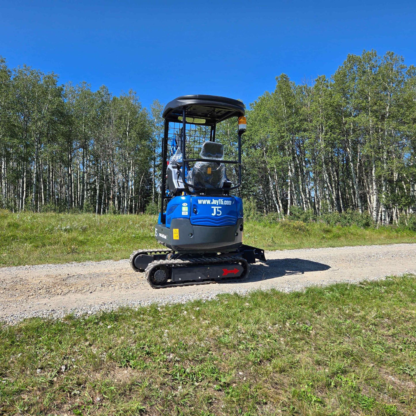 Rippa R15 Mini Excavator For Sale – rear view of compact excavator on countryside gravel road with forest background.