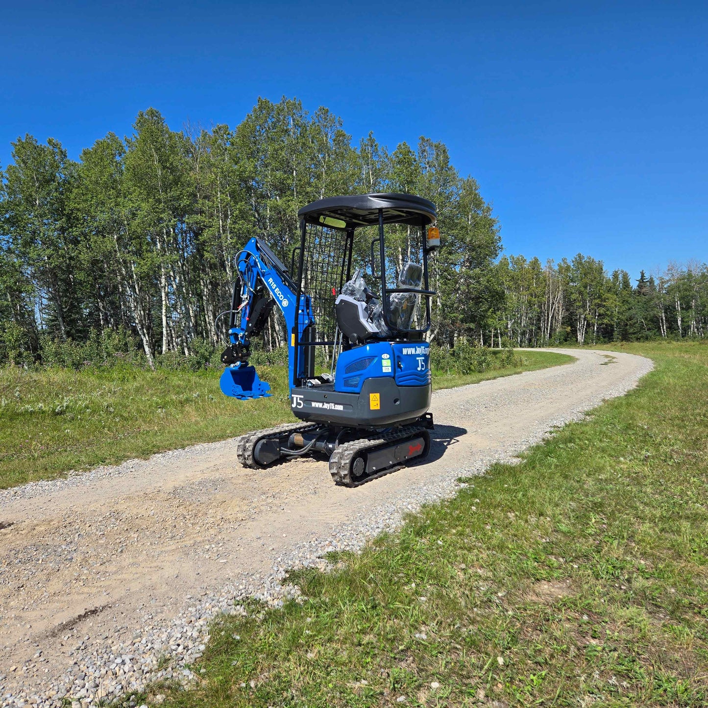 Rippa R15 Mini Excavator For Sale – side view of compact digger on rural gravel road with green forest background.