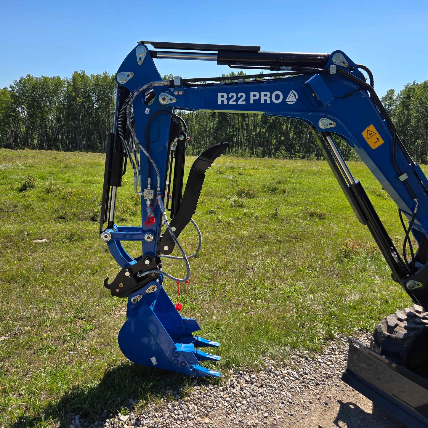 Side view of Rippa R22 Mini Excavator for sale showing boom, arm, hydraulic thumb, and digging bucket attachment in a grassy field.