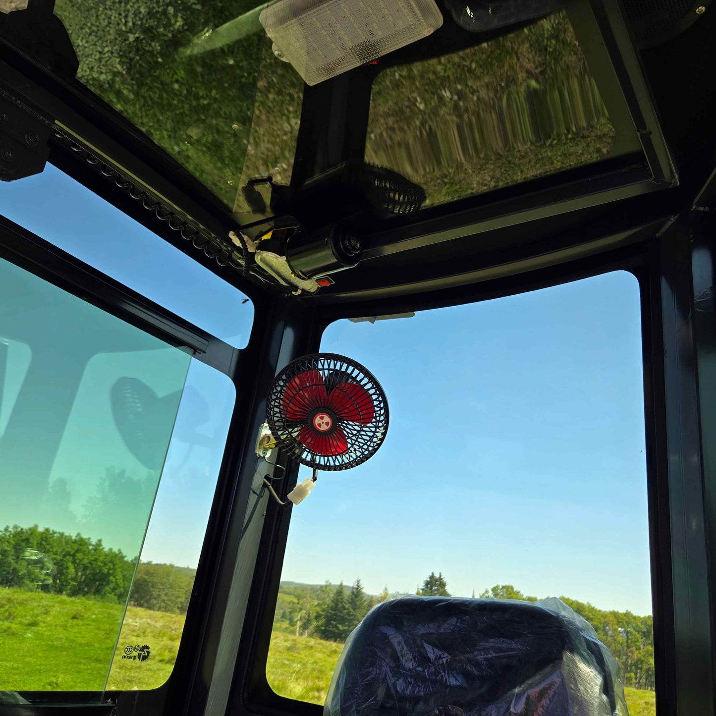 Inside view of Rippa R22 Mini Excavator for sale cabin showing seat, mounted fan, glass windows, and clear outdoor scenery.