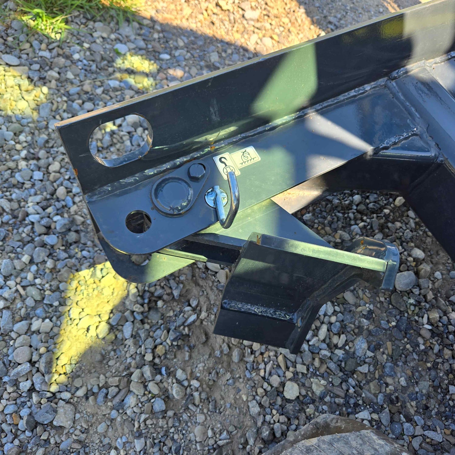 Close-up view of the dozer blade on the Rippa R22 Mini Excavator, for sale showing metal frame, welded joints, and safety pin on gravel ground.