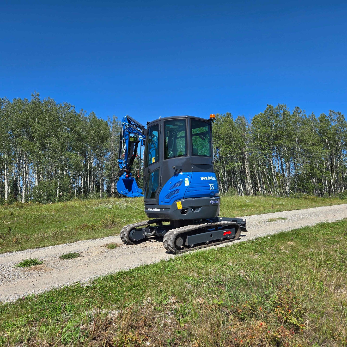 Side rear view of the Rippa R22 Mini Excavator for sale parked on a dirt road with trees in the background.