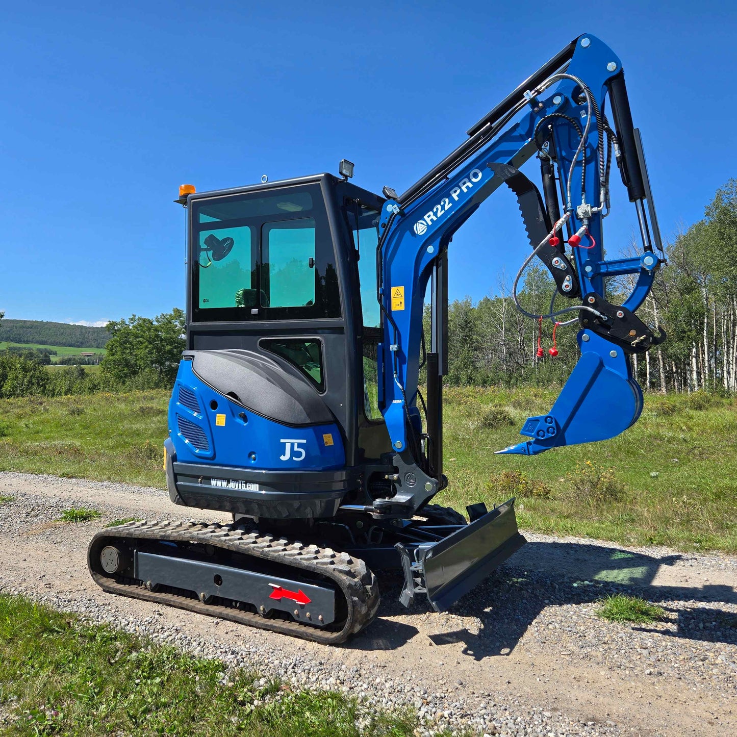 Side view of Rippa R22 Mini Excavator for sale with bucket raised, parked on a gravel path in a green field.