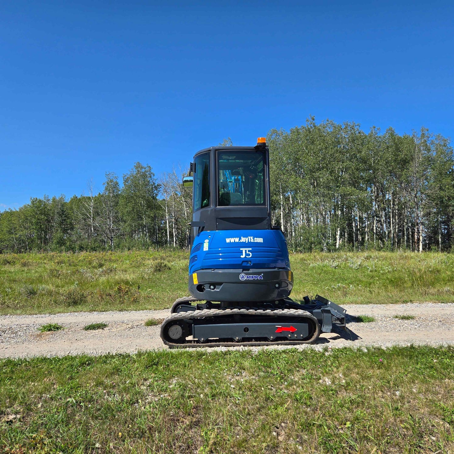 Straight rear view of the Rippa R22 Mini Excavator for sale on a dirt path with trees and grass in the background.