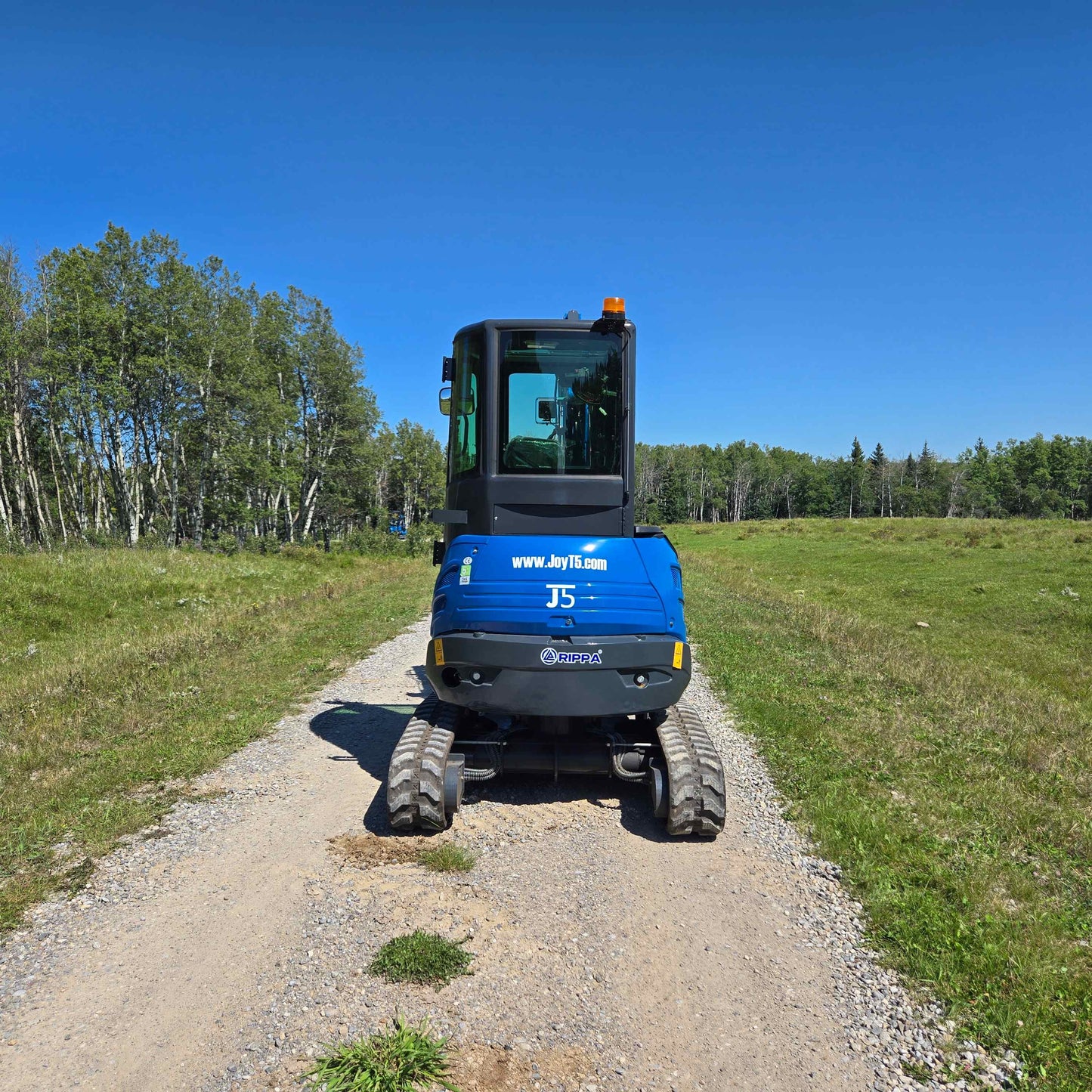 Rear view of Rippa R22 Mini Excavator for sale on gravel path with trees and grass field in the background.