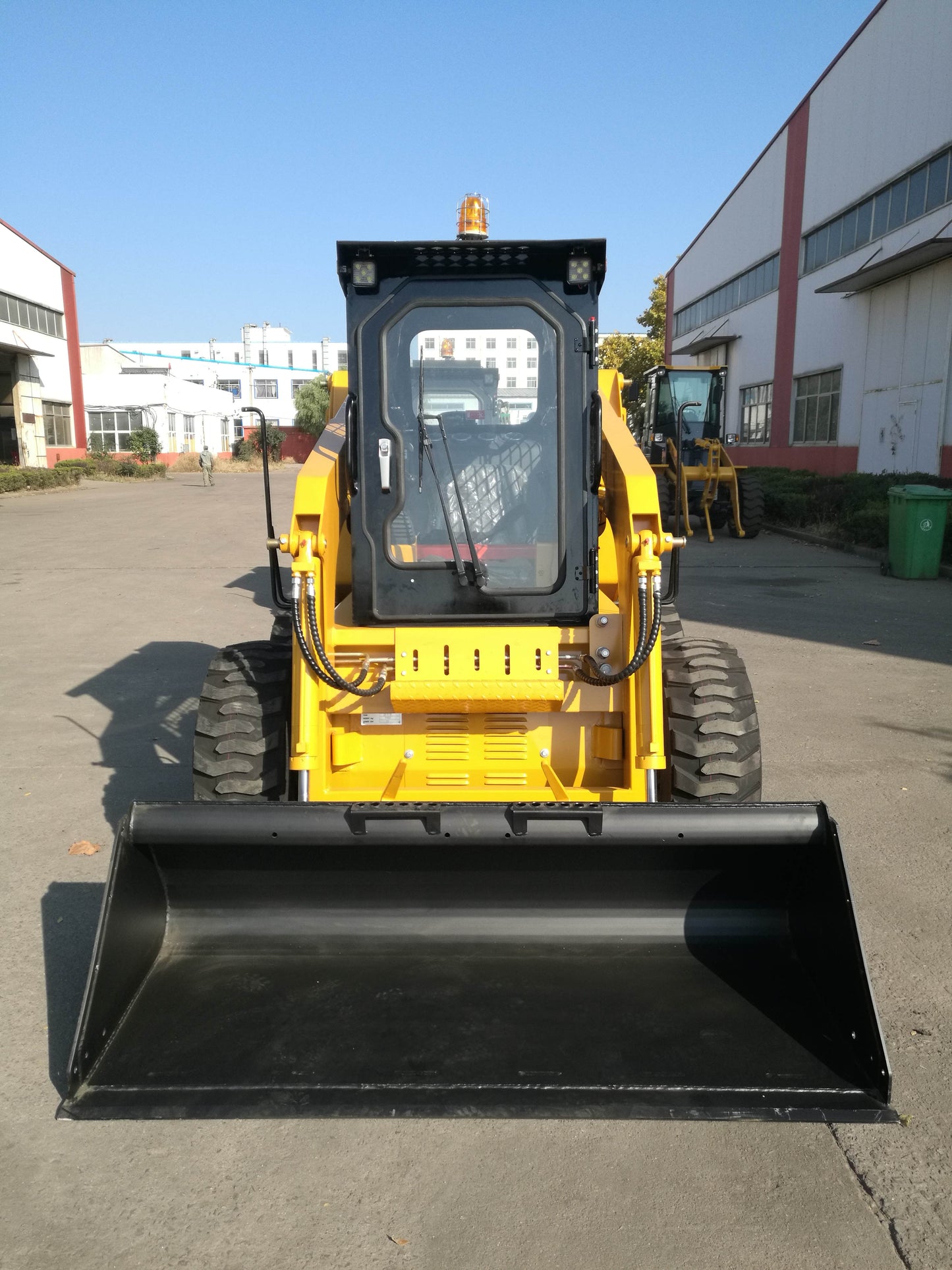 Yellow wheeled skid steer loader front view with large bucket attachment parked on pavement outside industrial buildings in Canada