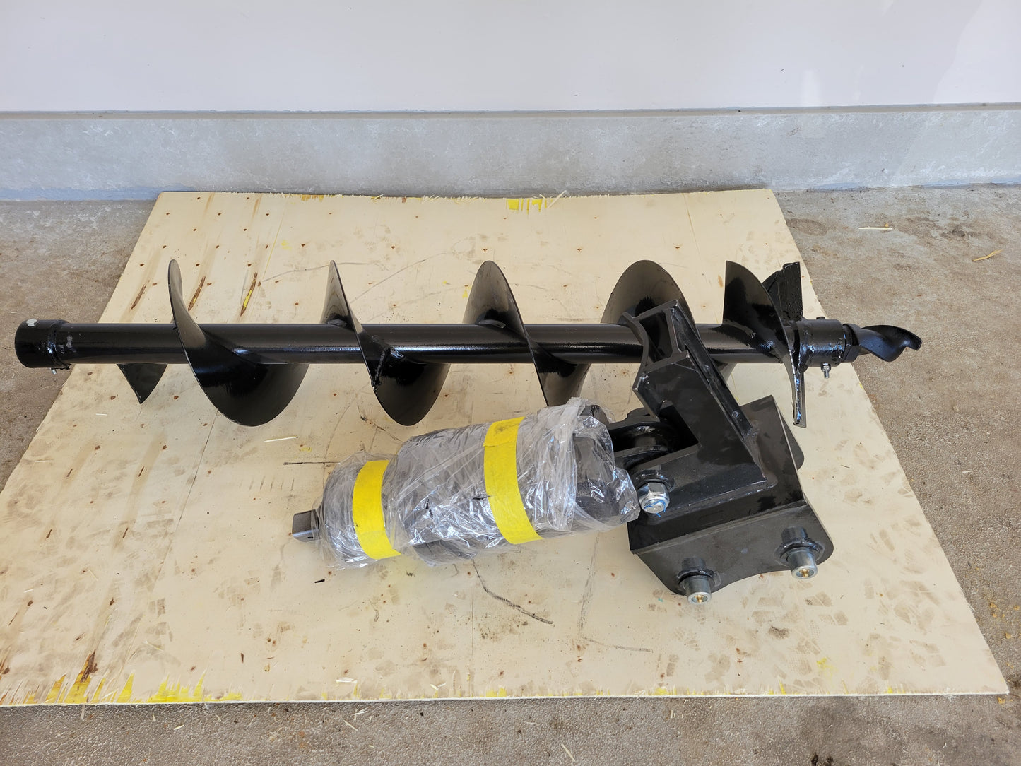 Hydraulic auger attachment for excavators by JoyT5, heavy-duty drilling tool placed on the ground, wrapped and ready for use.