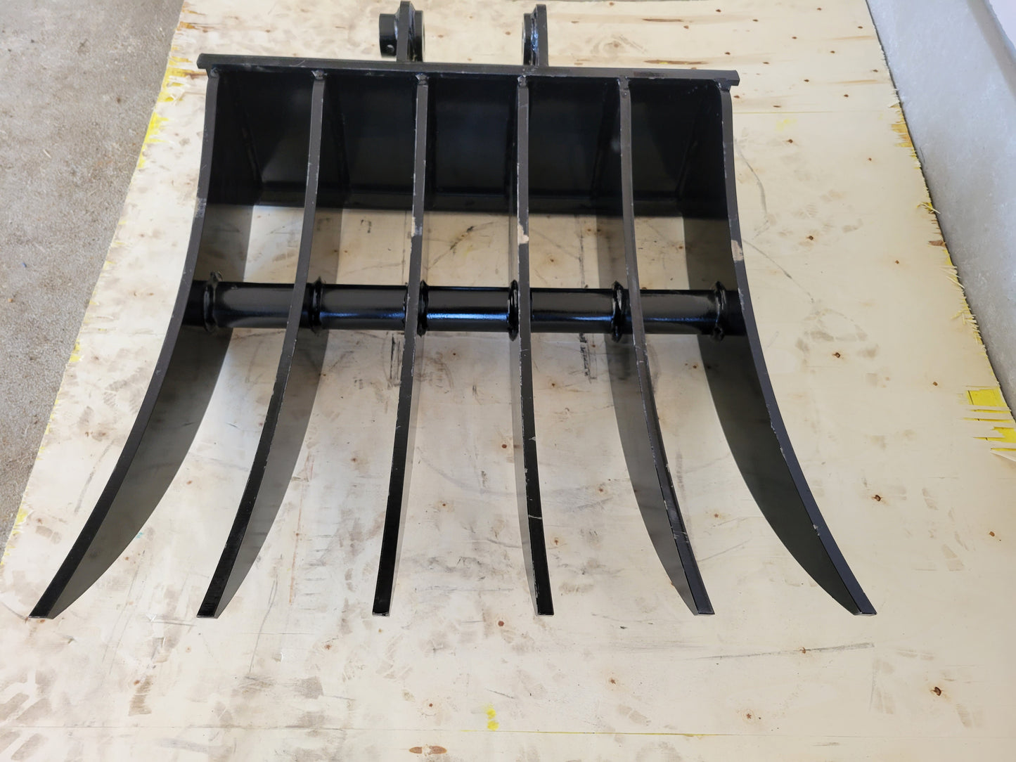 Mini excavator rake attachment front angle showing strong curved steel tines for heavy duty landscaping site cleanup and debris removal in Canada