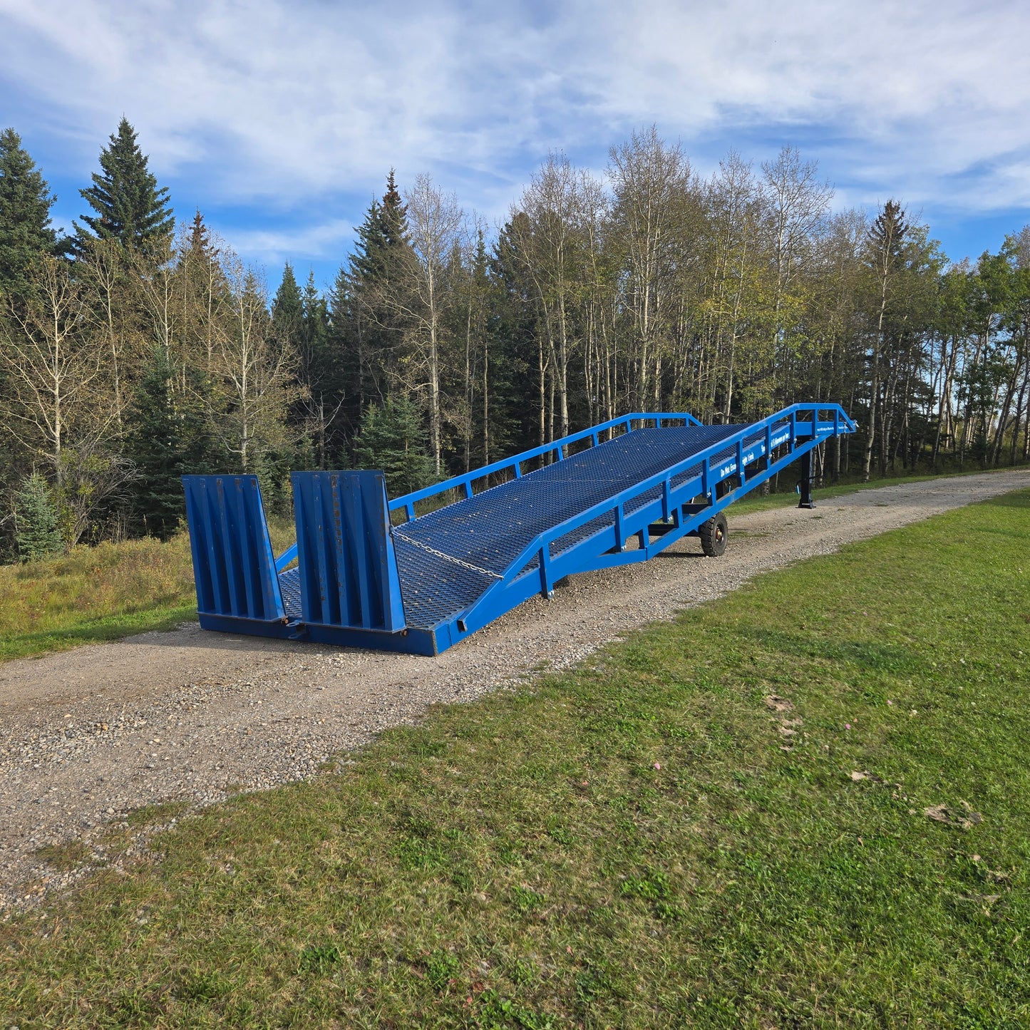 Twelve ton blue steel mobile loading ramp positioned outdoors on gravel surface in Canada used for forklift and truck container loading operations