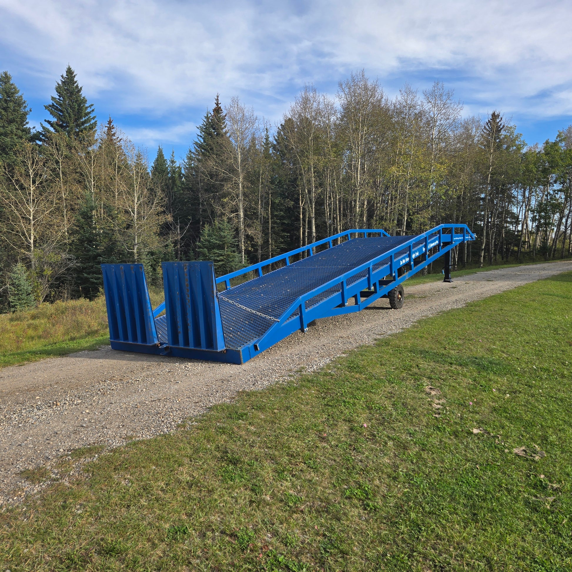 Twelve ton blue steel mobile loading ramp positioned outdoors on gravel surface in Canada used for forklift and truck container loading operations