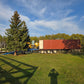 Yellow forklift loading a large container truck using a blue twelve ton mobile loading ramp on an open grass field in Canada under clear blue sky

