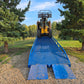 Yellow forklift driving up twelve ton blue steel mobile loading ramp surrounded by green trees used for truck and container loading in Canada

