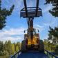 Yellow forklift front view driving up blue twelve ton mobile loading ramp with raised bucket against clear sky and green trees in Canada

