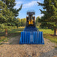 Yellow forklift front view driving up a blue twelve ton mobile loading ramp placed on gravel surface between green trees in Canada

