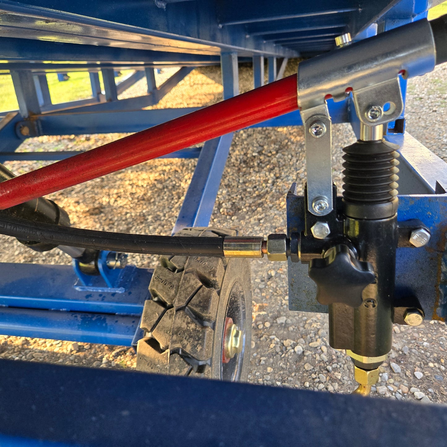 Close up view showing hydraulic valve control system with red handle and hose connection under blue mobile loading ramp for forklift use in Canada

