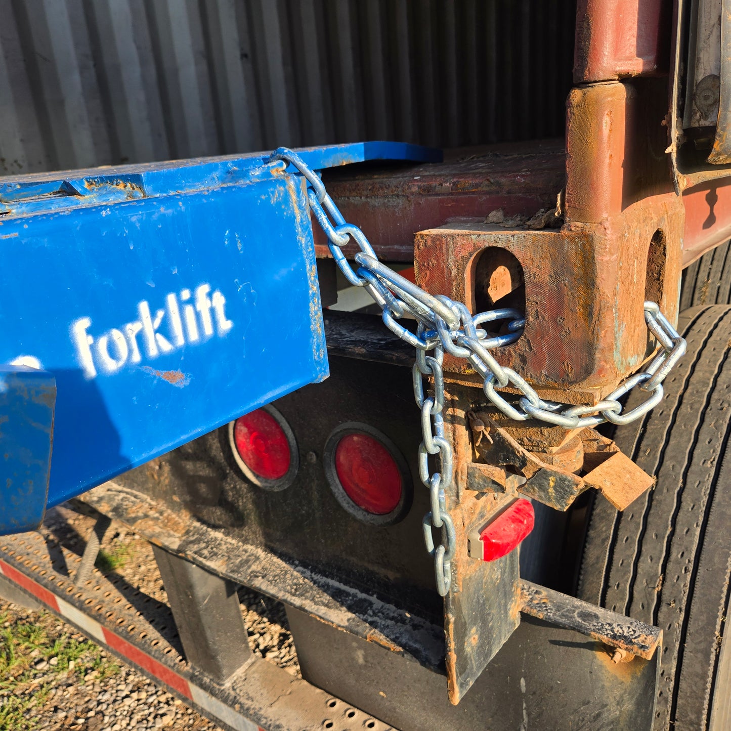 Close up view showing safety chain connection between blue steel mobile loading ramp and truck container for forklift loading in Canada