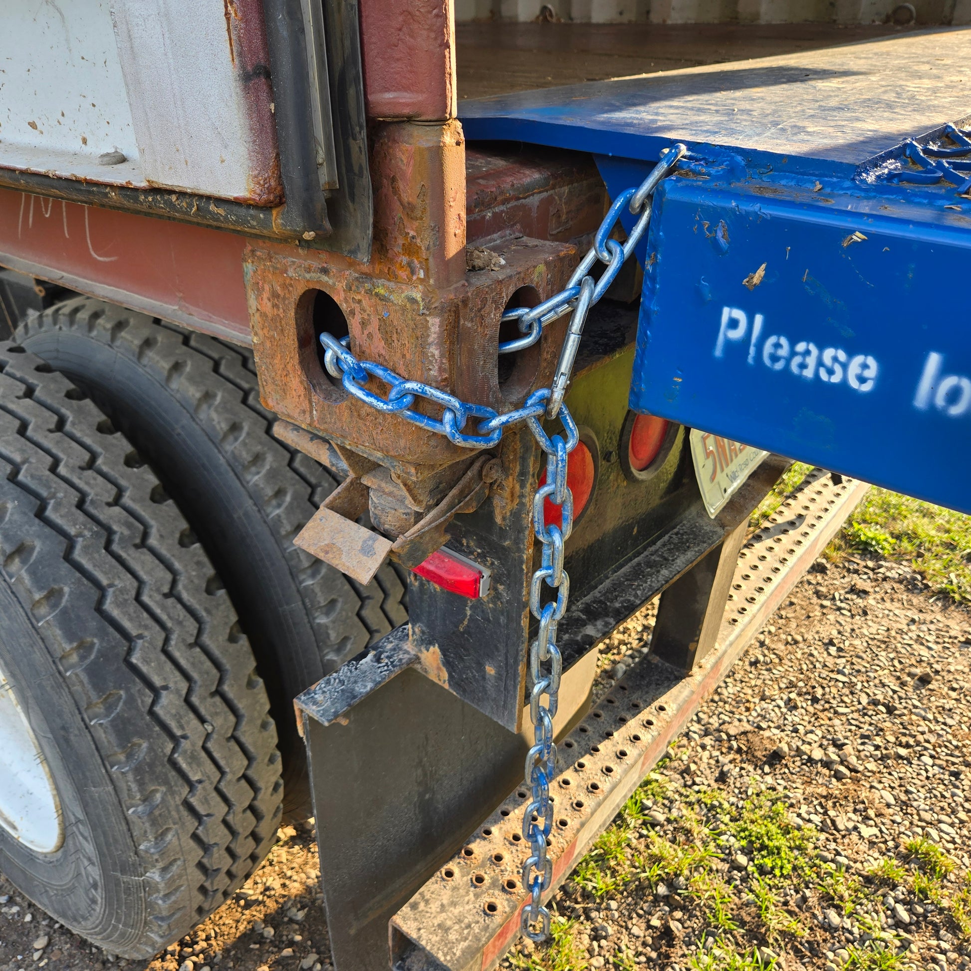 Close up view showing heavy duty safety chain securely connecting blue steel mobile loading ramp to truck container for forklift loading in Canada

