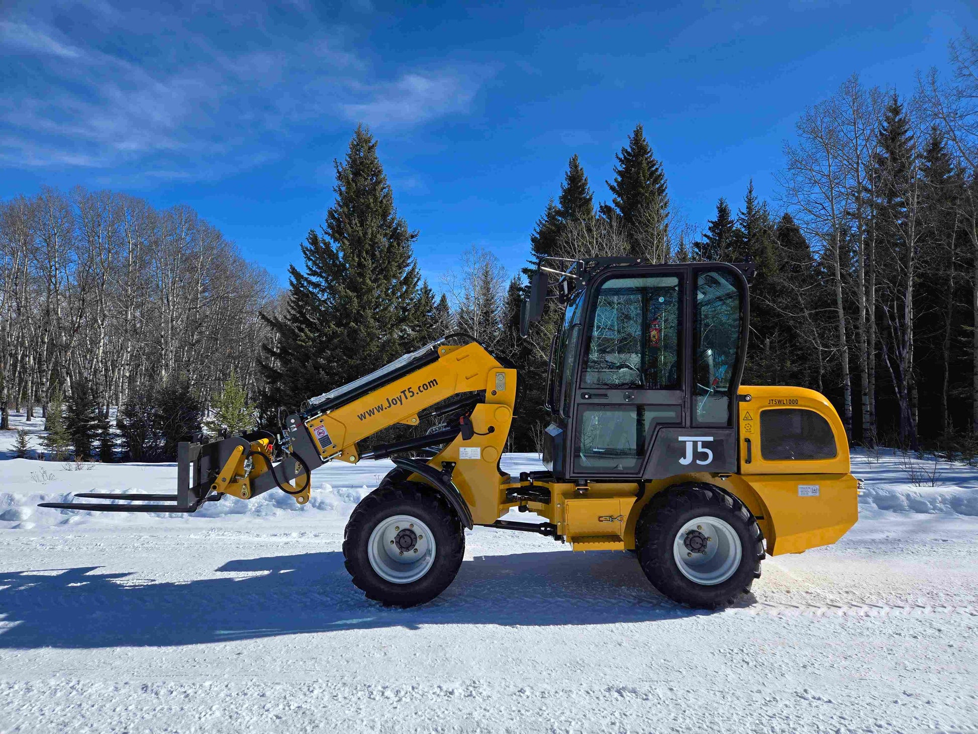 JT5WL1000 compact wheel loader 1 ton 2200 lbs side profile view with pallet fork attachment on snowy field.