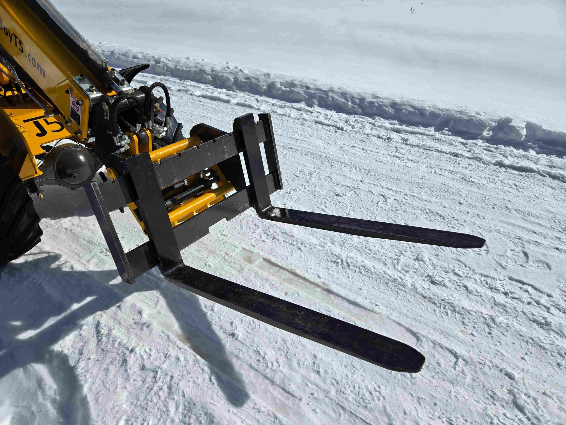 Close-up view of JT5WL1000 compact wheel loader 1 ton 2200 lbs pallet fork attachment on snowy ground