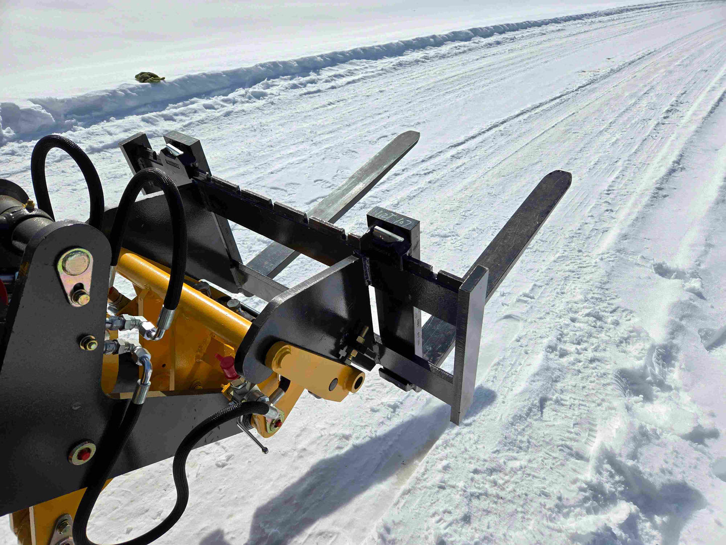 Close-up of JT5WL1000 compact wheel loader pallet fork attachment with hydraulic system on snowy road