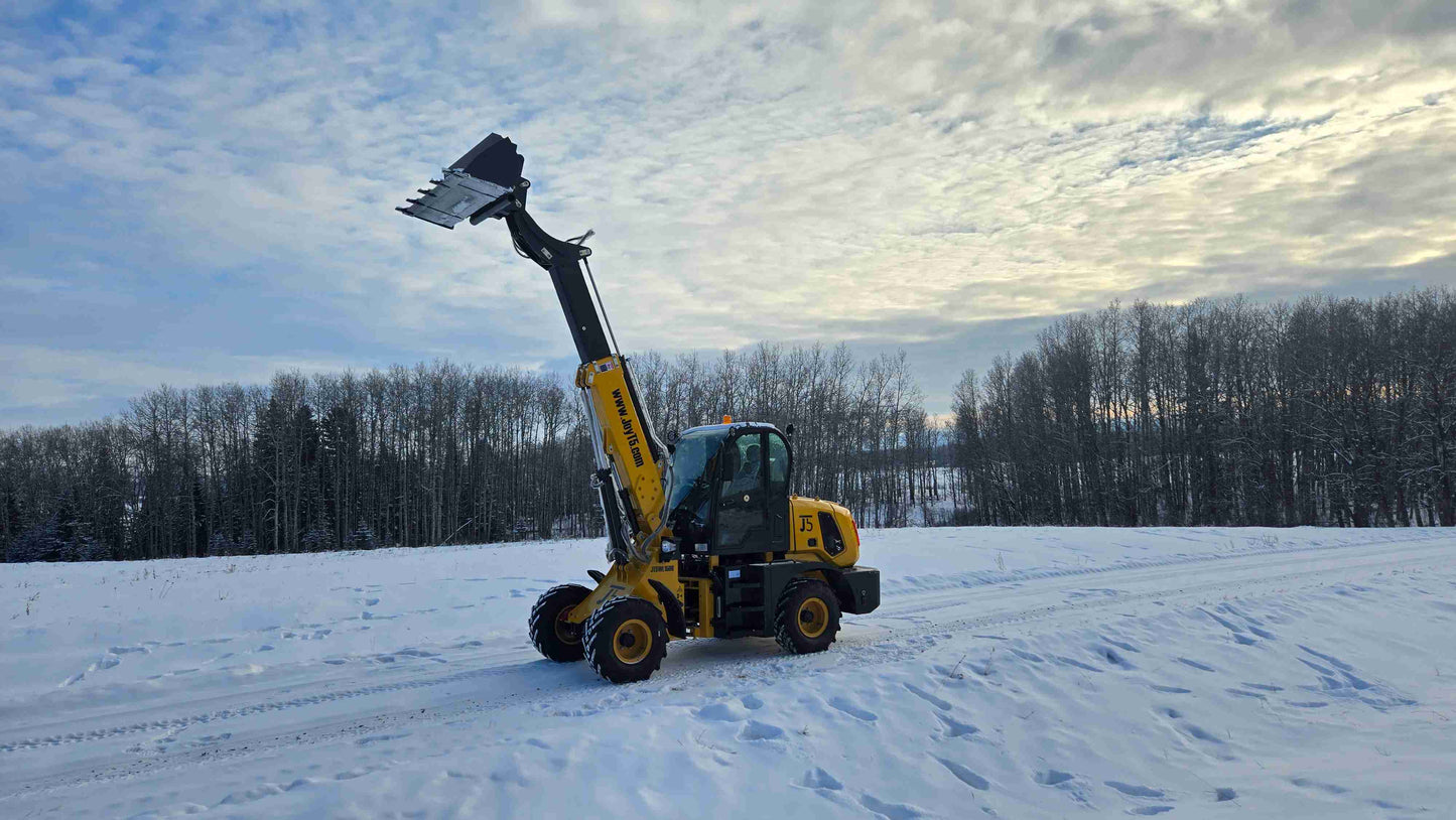 JT5WL1500 compact wheel loader with extended boom and raised bucket on snow-covered field.