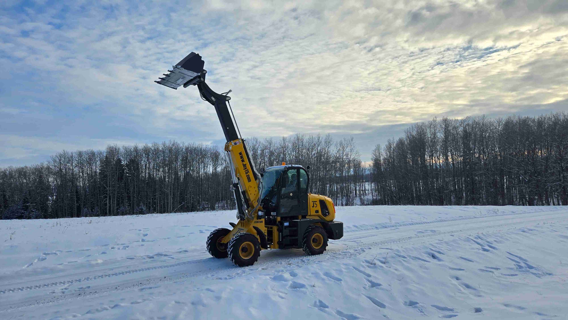 JT5WL1500 compact wheel loader with extended boom and raised bucket on snow-covered field.
