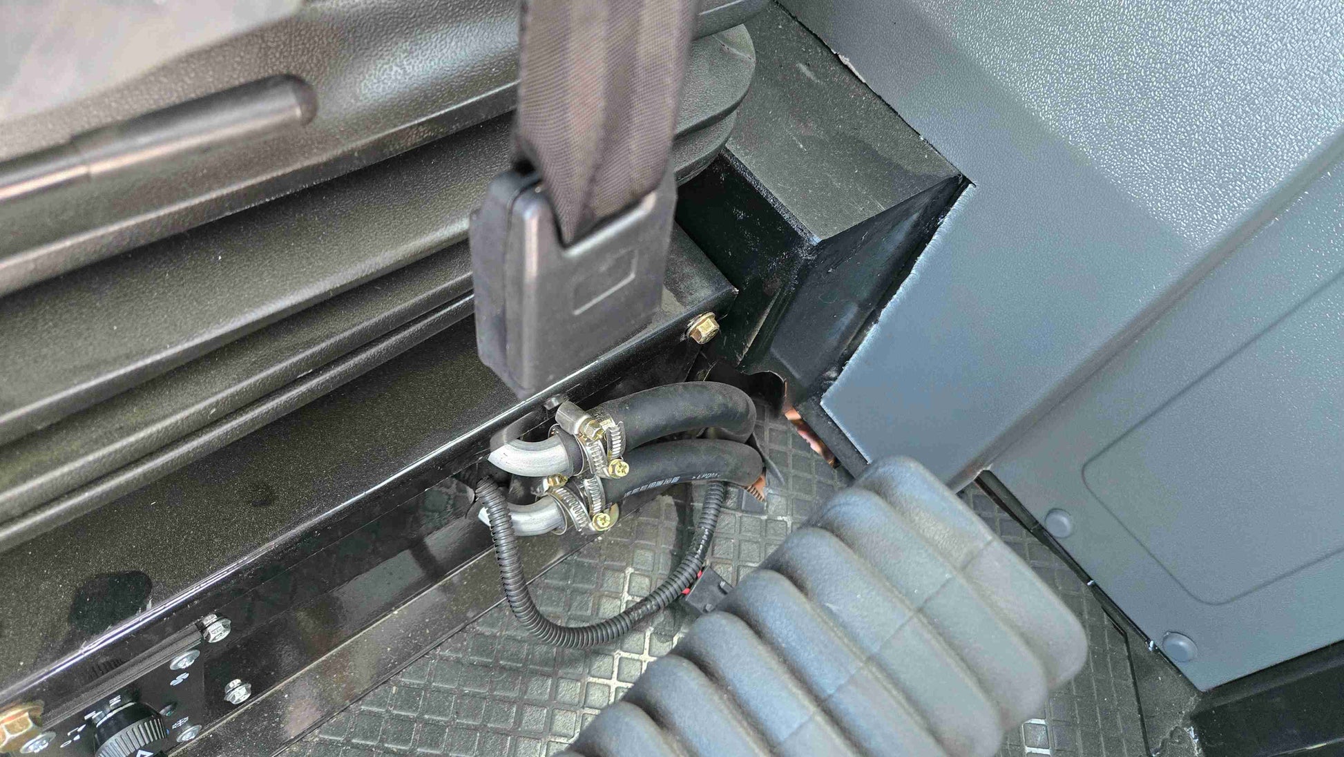 Close-up of JT5WL1500 compact wheel loader cabin showing seat belt lock, secure hydraulic hoses, and pedal with anti-slip floor design.