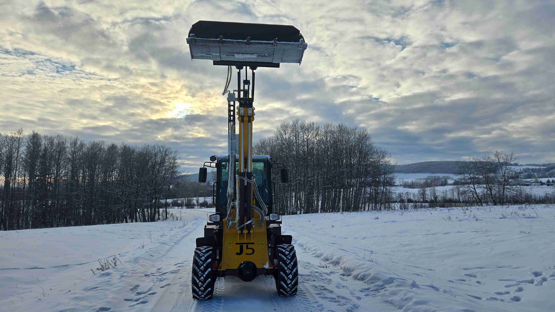 JT5WL1500 compact wheel loader front view with bucket raised high in snowy Canadian construction site.