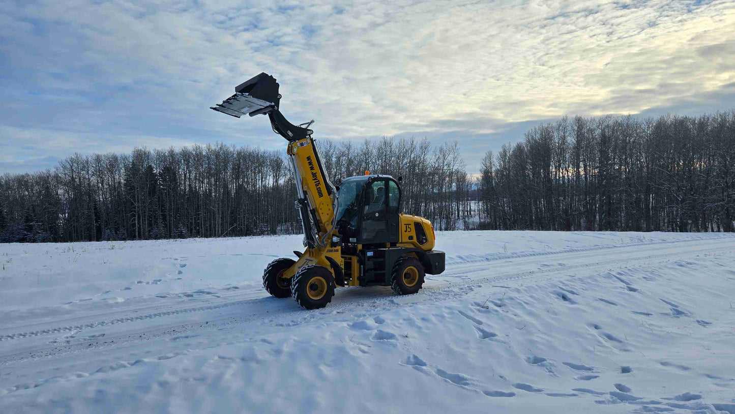 JT5WL1500 compact wheel loader front view with raised bucket working in snowy Canada construction site.