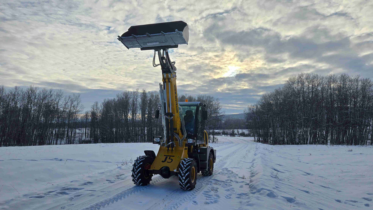 JT5WL1500 compact wheel loader front view with fully raised bucket on snowy construction site in Canada.