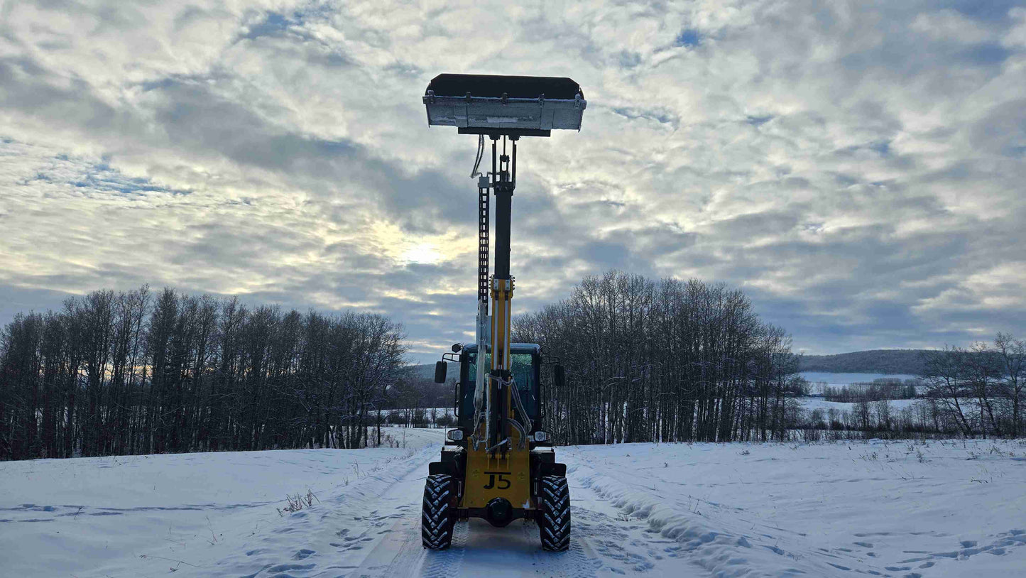 JT5WL1500 compact wheel loader front view with fully raised boom and bucket at maximum height in snowy field.