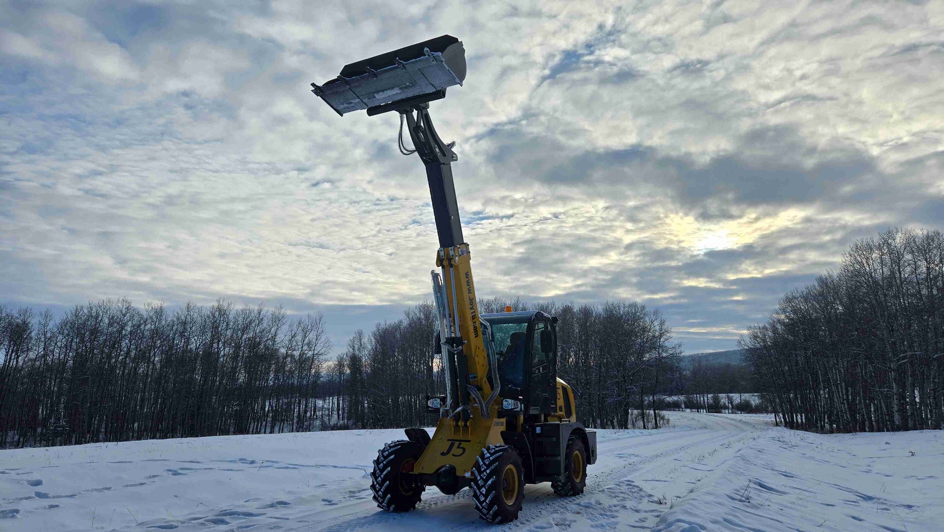 JT5WL1500 compact wheel loader front view with fully extended boom and raised bucket on snowy ground.