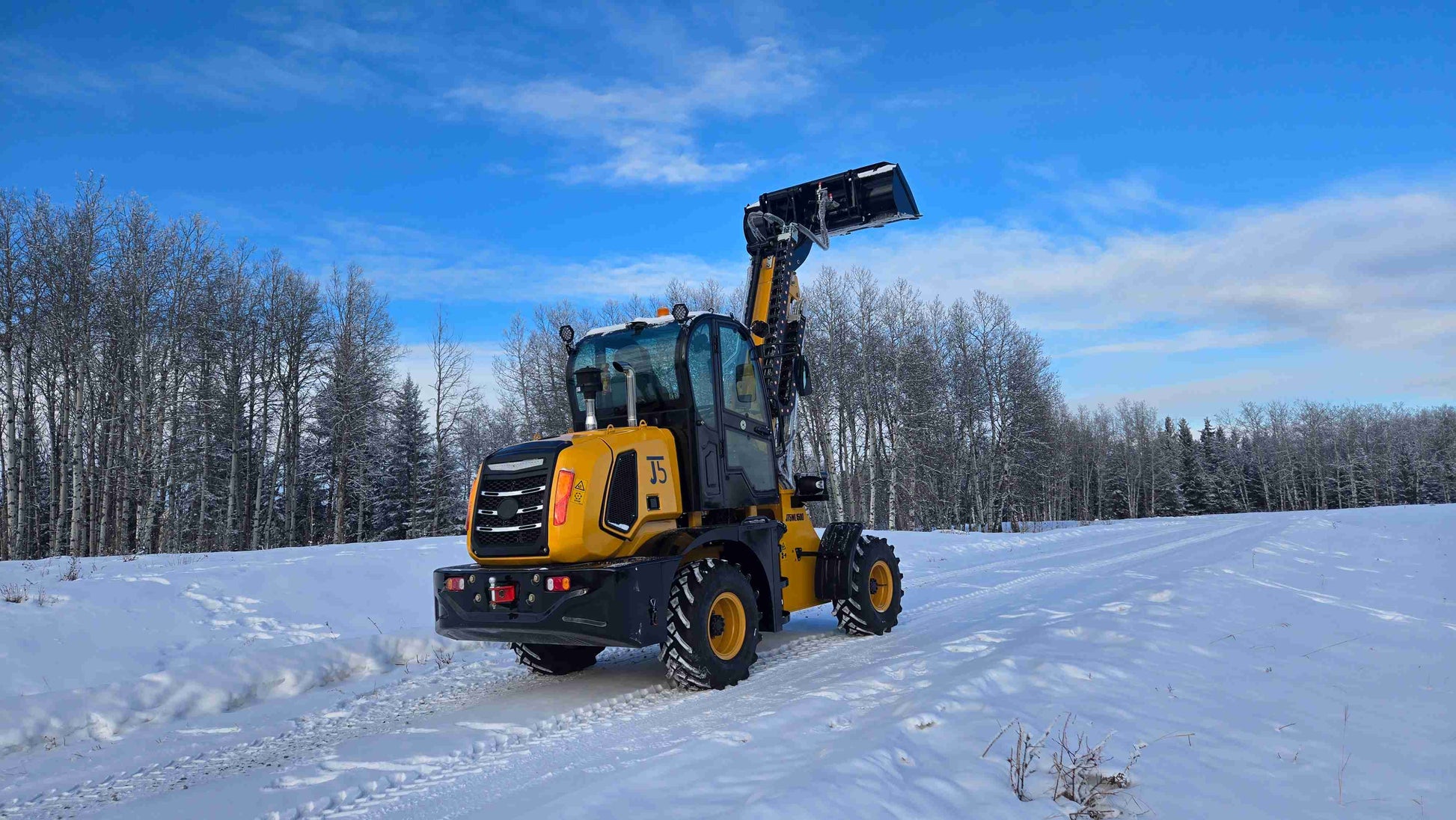 JT5WL1500 compact wheel loader rear three-quarter view with bucket lifted upright on snowy terrain.