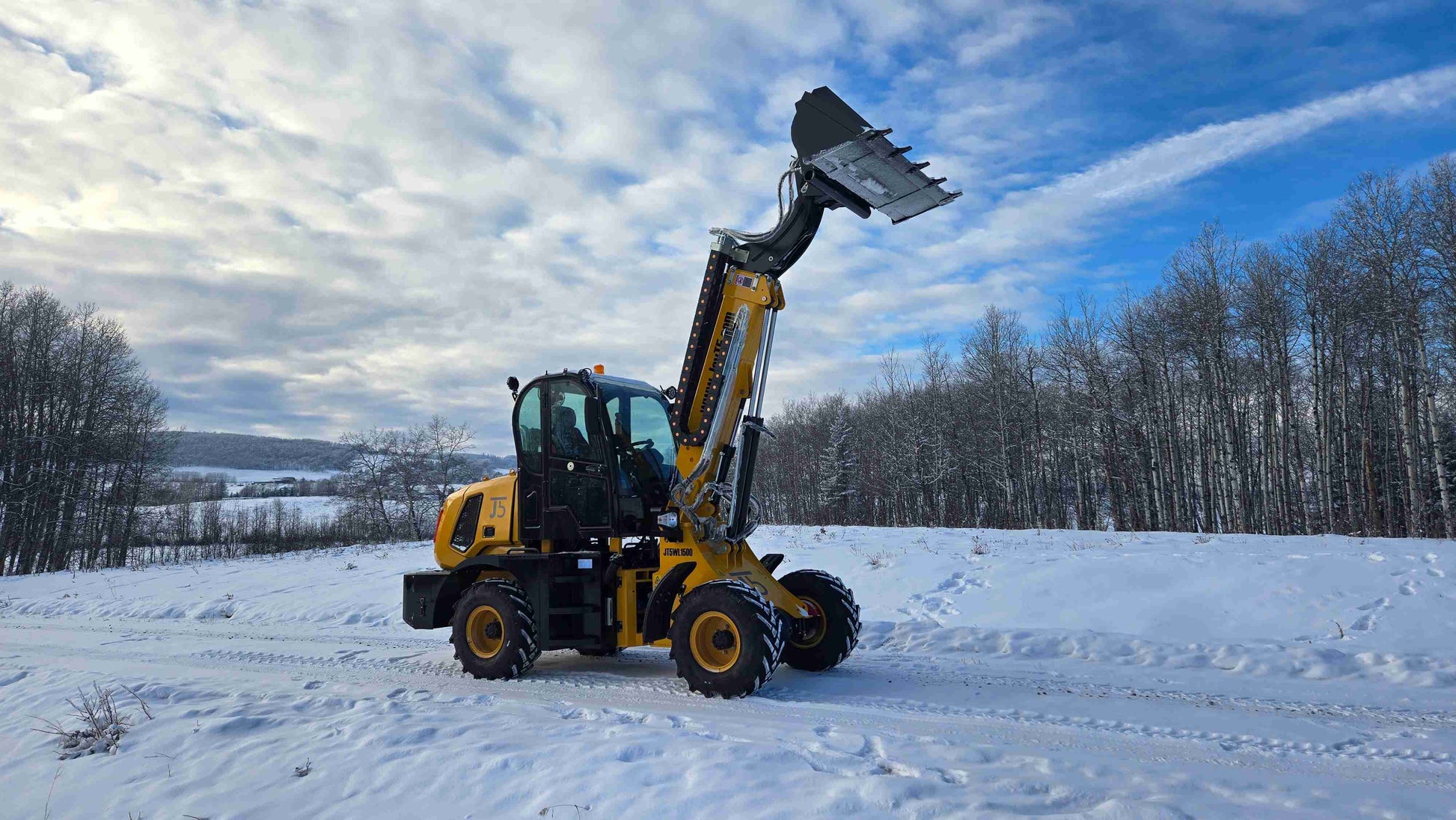 JT5WL1500 compact wheel loader side view with bucket raised and tilted in snowy Canadian construction site.