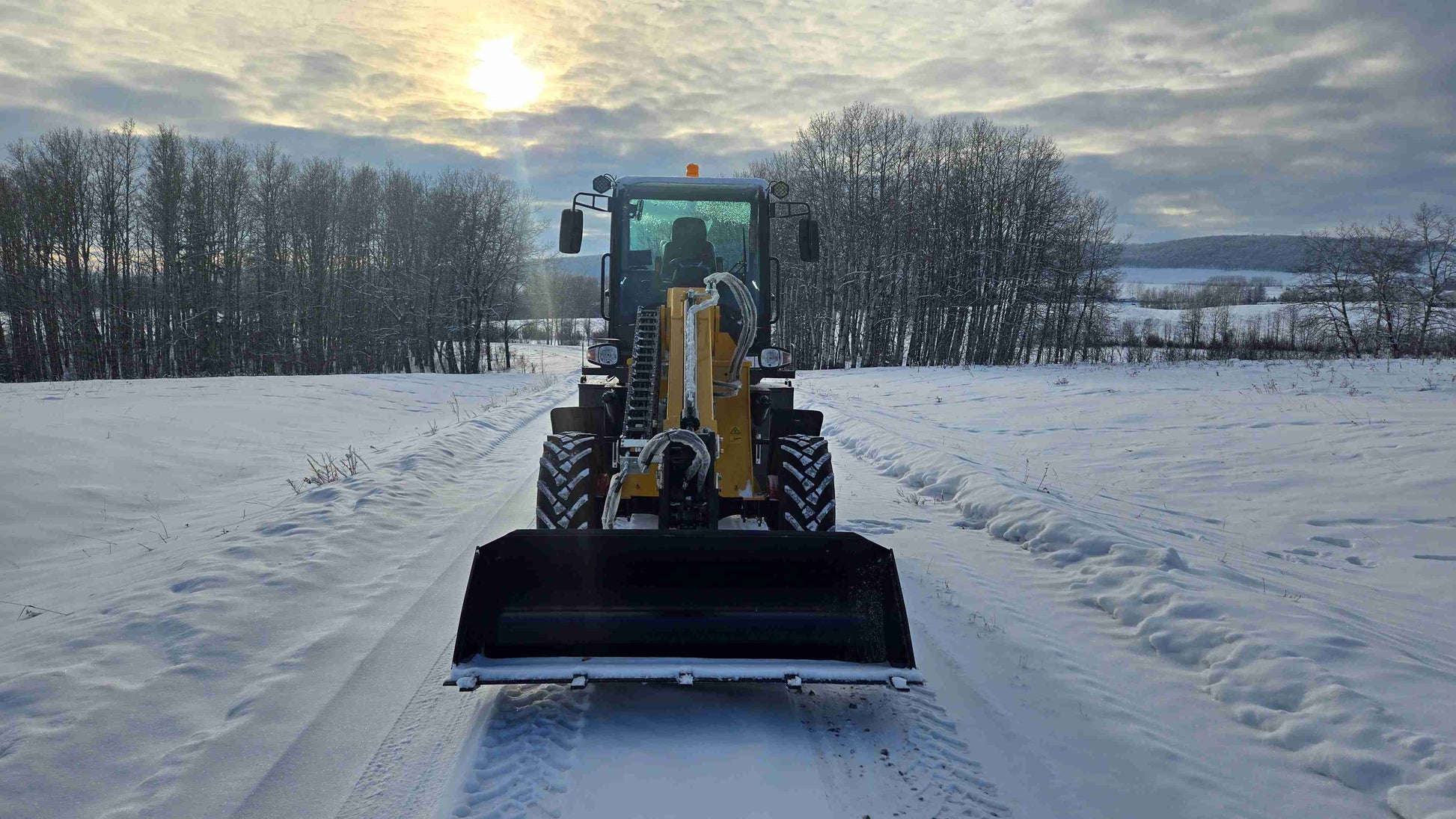 JT5WL1500 wheel loader front view with bucket lowered on snowy terrain during sunrise.