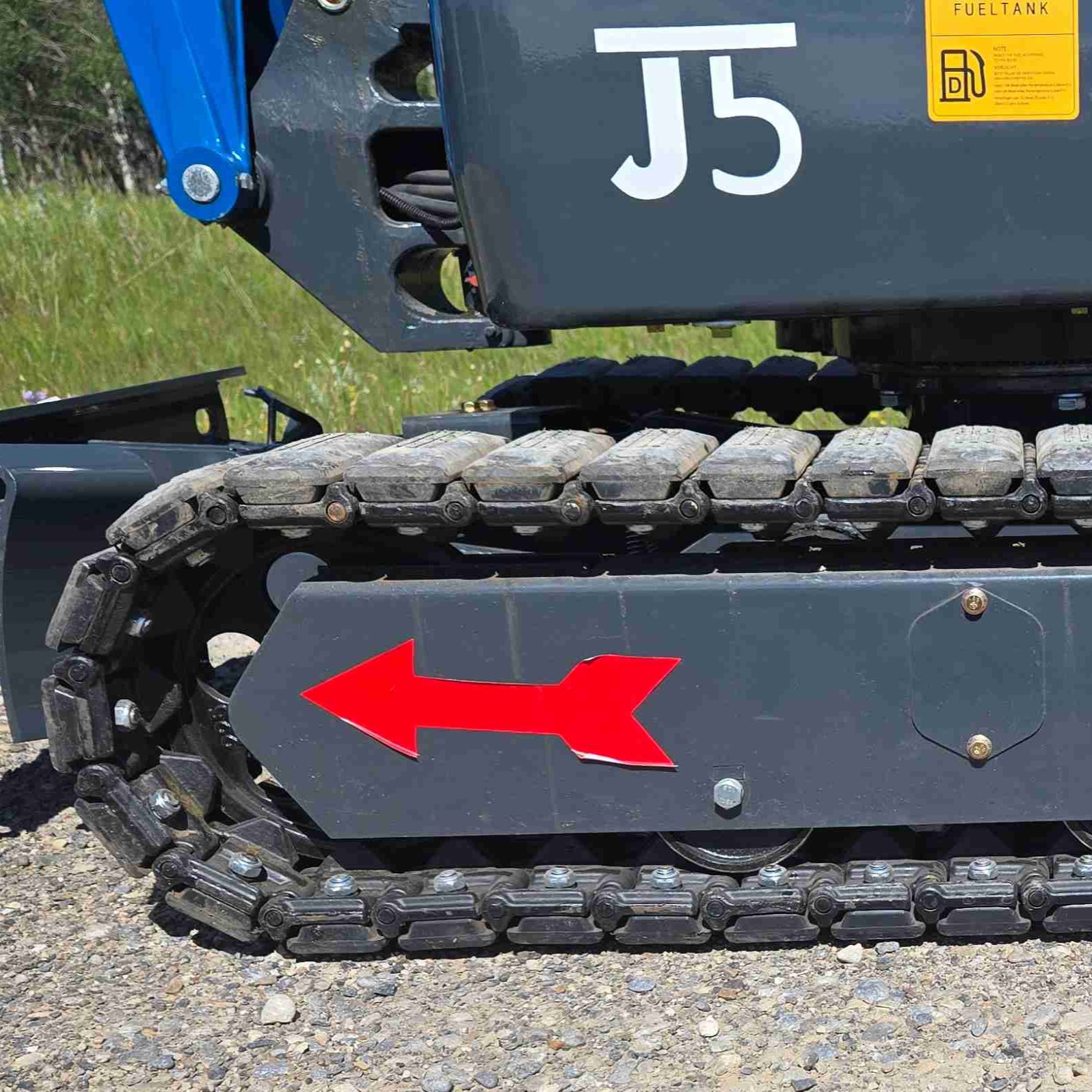 Close-up of metal tracks on a Rippa R13 mini excavator for sale by JoyT5 with a red arrow and JoyT5 branding on a grassy background.