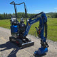 Rippa R13 mini excavator for sale by JoyT5 on a gravel road with green fields and trees in the background